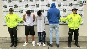 Se aprecian dos fotografías, en una de ellas hay tres hombres, uno de ellos de espaldas a la cámara. Uno viste camiseta blanca de manda ziza, bermuda negra y zapatillas blancas; otyro viste camiseta de manga corta blanca, jean azul uy zapatillas blancas con negro y el tercero buso azul con capucha, jean azul claro y zapatos negros. A los extremos hay uniformados de la Policía Nacional y en la parte posterior hay un pendón institucional de la Policía. En la fotografía 2 hay un hombre que viste camiseta negra de manga corta y vermuda gris con manchas negras y zapatos negros. A sus extremos hay uniformados de la Policía y detrás de ellos hay un pendón de la Policía.