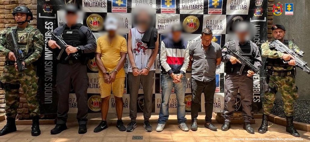 En la fotografía se aprecia de pie, con los brazos atrás y mirando al piso a Luis Carlos Vásquez Vanegas. Viste camisa de manga corta de color gris, pantalón oscuro y zapatos negros. A sus extremos hay servidores del CTI de la Fiscalía y del Ejército. Detrás de ellos hay un pendón con logos del Gaula Militar y de la Fiscalía.