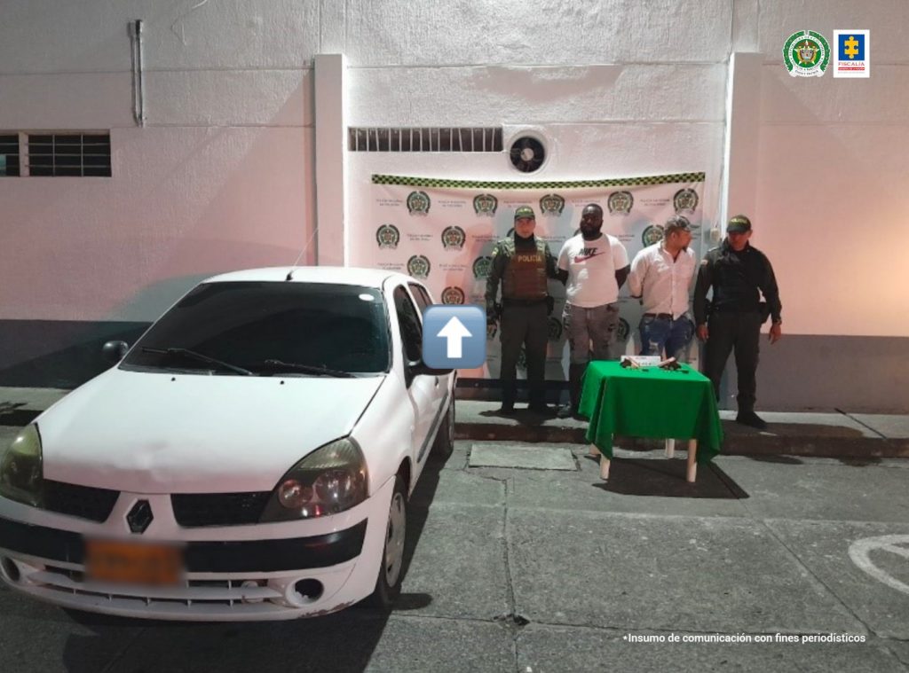 En la foto aparecen de pie, Mauricio Alexánder Monsalve Buriticá y Yeison Stiven Castillo Ocoró. Uno de ellos, de tez negra, viste camiseta blanca de manga corta y jean. El otro, viste camisa blanca de manga larga y jean. A lado y lado de ellos hay uniformados de la Policía Nacional. Delante de ellos se aprecia un vehículo particular blanco, una mesa con mantel verde y sobre ella hay dos armas de fuego y munición. Detrás de ellos hay un pendón institucional de la Policía.