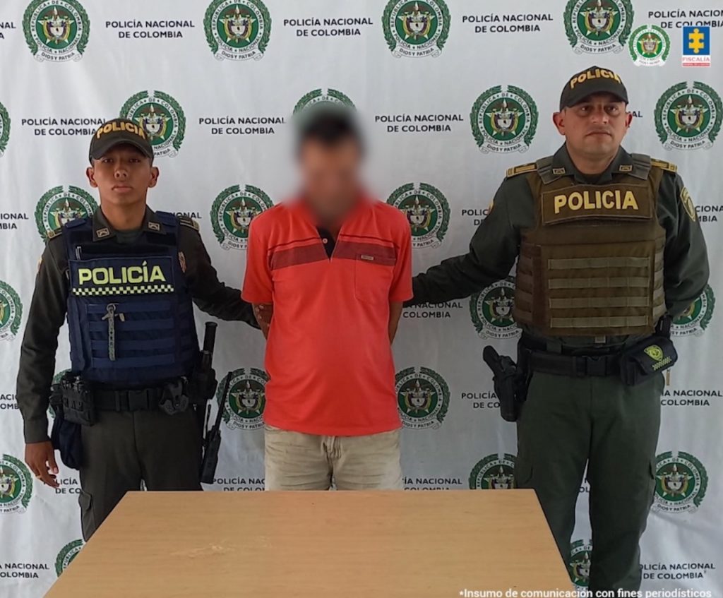 En la imagen aparece una persona de suéter naranja, entre dos uniformados de la Policía.