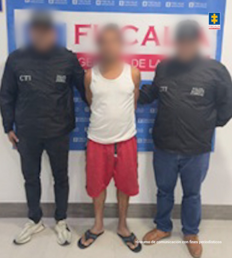 En la imagen aparece una persona de pantaloneta roja y camiseta blanca, entre dos uniformados del CTI.