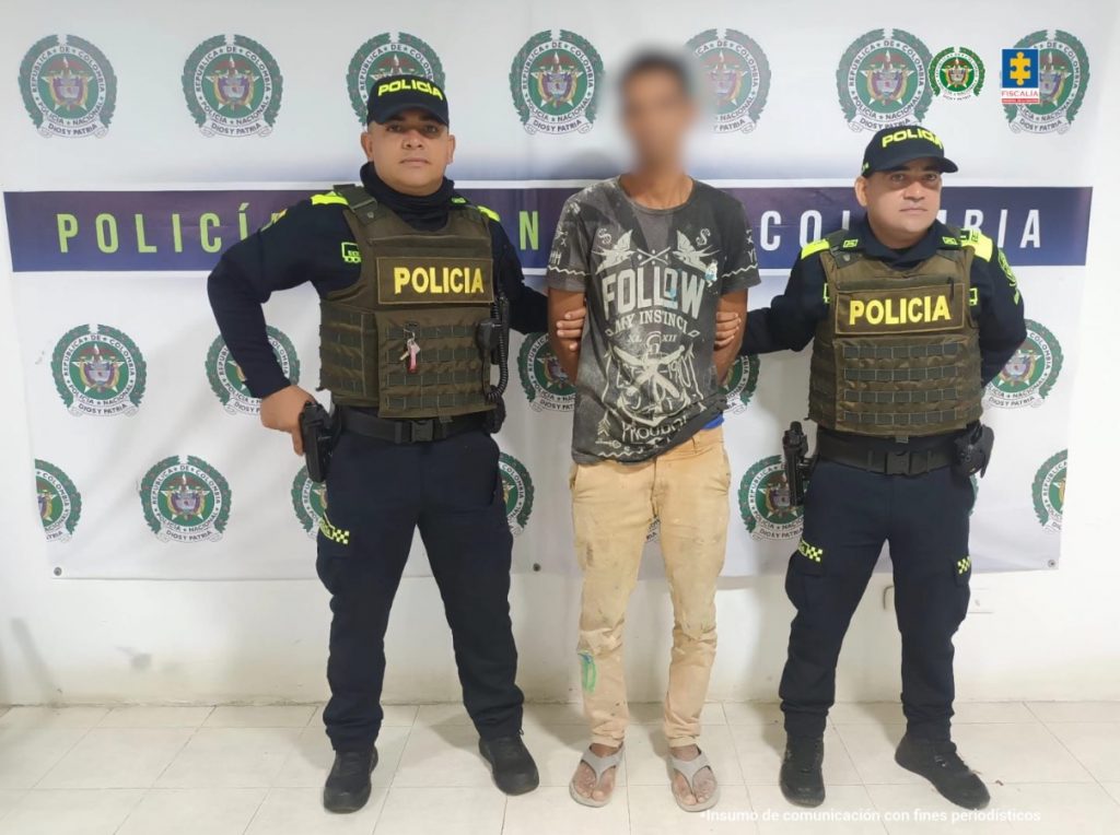 En la imagen aparece una persona de suéter gris, entre dos policías.