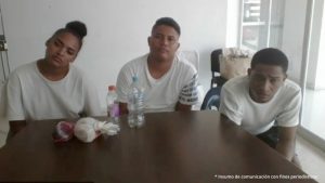En la imagen están dos hombres, vestidos de camiseta roja y blanca con una mujer que tiene camiseta negra. Se encuentran sentados frente a una mesa escuchando la audiencia en la que se les procesó.