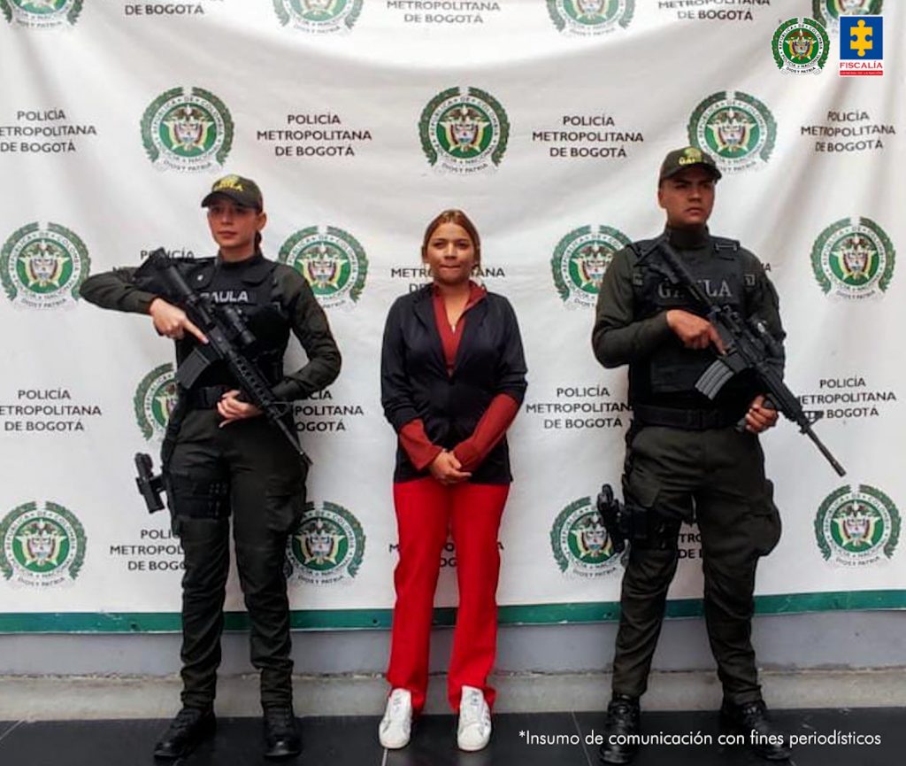 En la imagen aparece una persona de pantalón y suéter rojo, entre dos uniformados de la Policía.