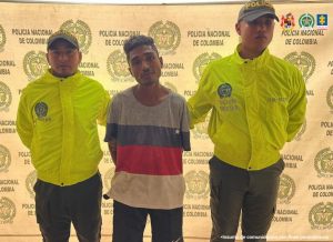 En la imagen aparece una persona de suéter blanco, con rojo y azul, entre dos uniformados de la Policía.