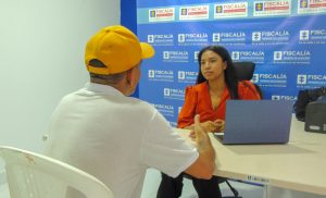 En la imagen se observa un funcionario de la Fiscalía frente a un usuario en una oficina.