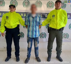 En la imagen aparece una persona de camisa de cuadros azules, entre dos uniformados de la Policía.