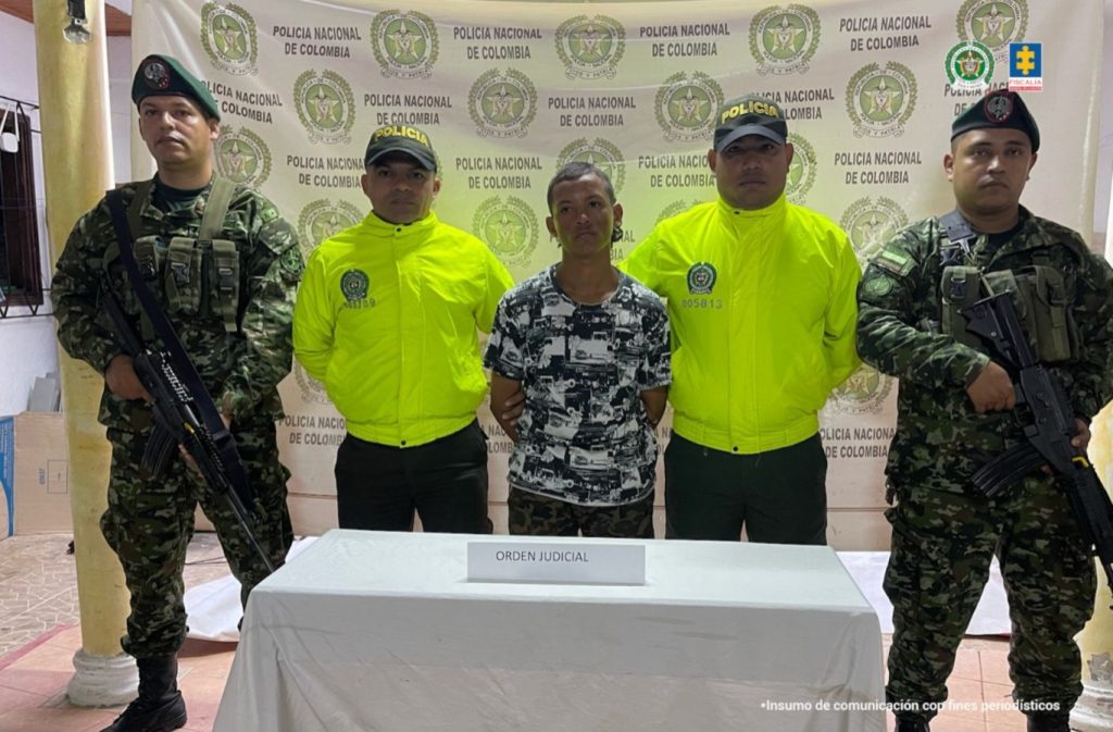 En la imagen aparece una persona de suéter blanco con negro, entre cuatro uniformados de la Policía.
