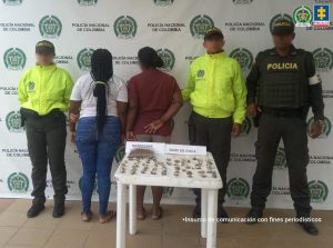 En la fotografía aparecen dos mujeres, gordas, de espalda oscura, esposadas, una con el pelo largo y negro suelto, trenzado y la otra con el pelo negro recogido. Están custodiados por dos uniformados de la Policía Nacional. Frente a ellos hay una mesa con la droga incautada.