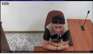 En la fotografía está un hombre trigueño, sentado frente a un escritorio de madera con un micrófono, vestido con una camiseta beige con negra en la sala de audiencia en la que se le procesó.