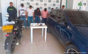En la fotografía aparecen los cinco capturados custodiados por dos agentes de la Policía Nacional. También se encuentra un automóvil azul, una motocicleta, el arma y la droga que se les incautó.