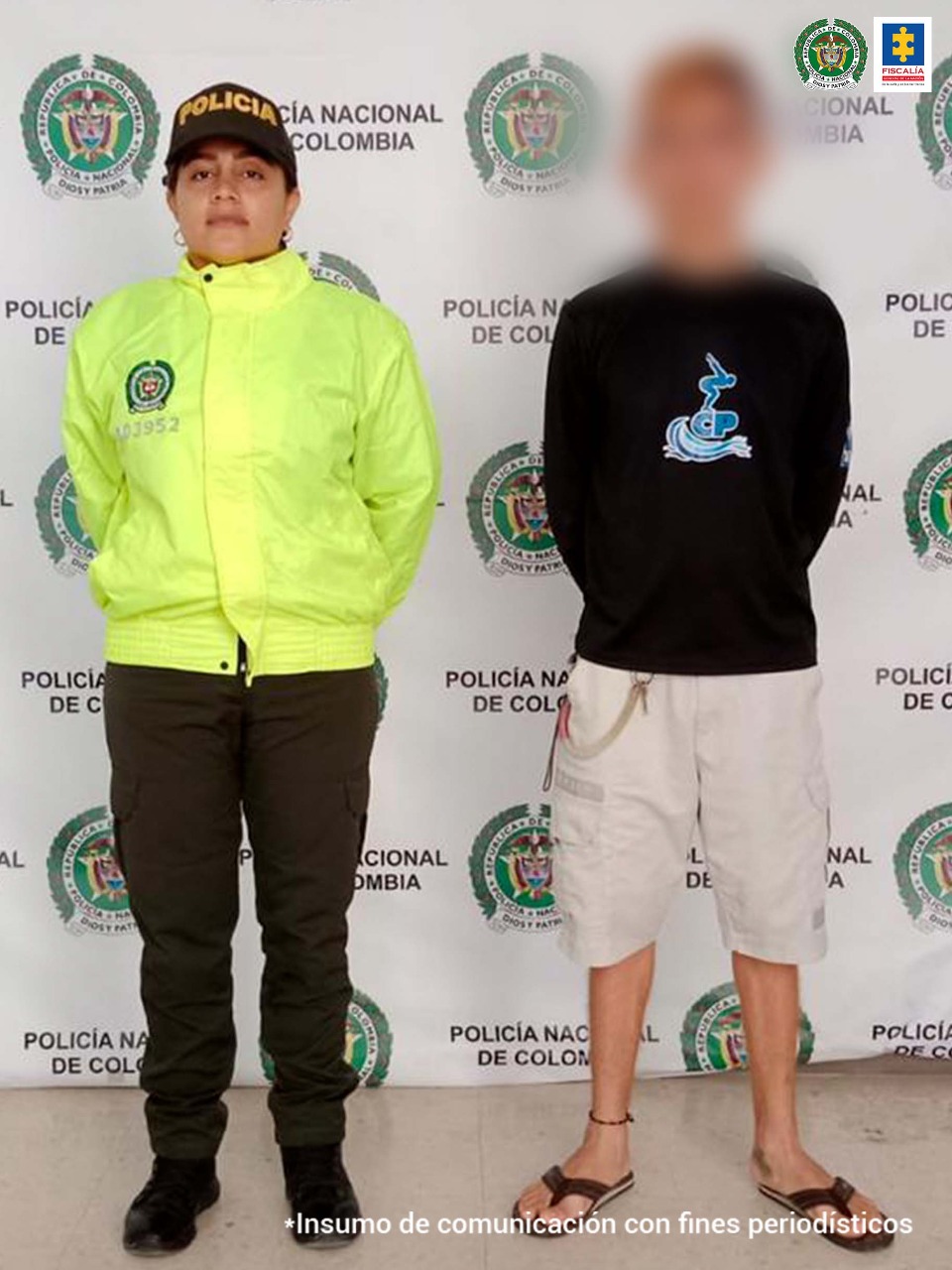 En la imagen se encuentra un hombre con buzo negro y bermuda beis, chanclas negras, custodiado por una uniformada de la Policía Nacional delante de un banner de la Policía Nacional.