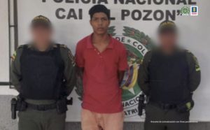 En la imagen aparece un hombre de camiseta blanca y bermuda verde, con dos uniformados de la Policia Nacional. Delante de ellos se encuentra una mesa con el arma cortopunzante con la que presuntamente cometió el homicidio.