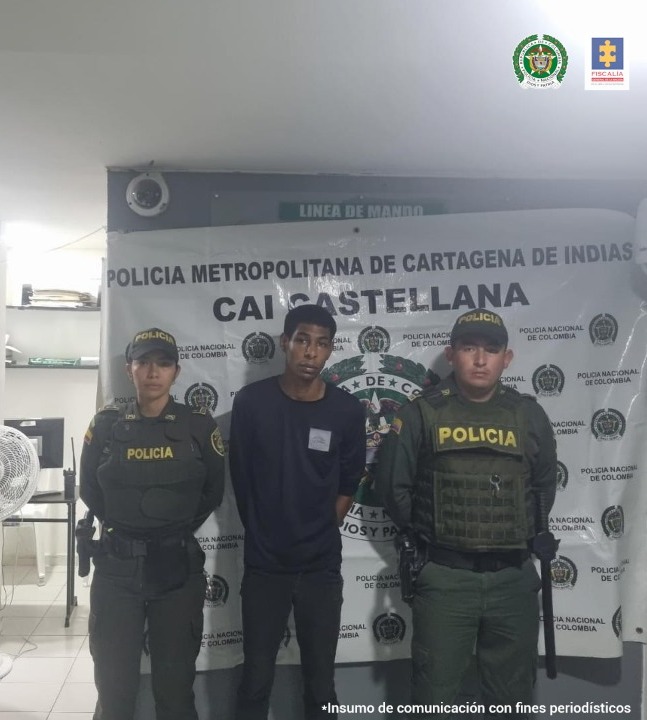 En la fotografía aparece un hombre con buzo negro y jean negro con dos miembros de la Policía Nacional, delante de un pendón de la Policía Nacional.