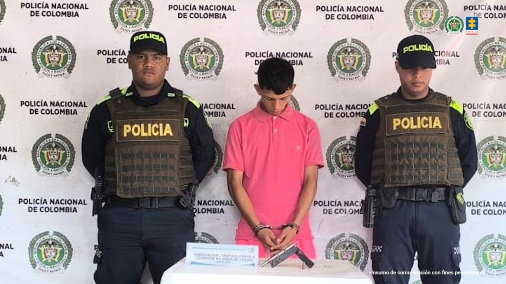 En la fotografía está un hombres, de frente, con las muñecas esposadas entre ellos, custodiado por dos uniformados de la Policía Nacional. Delante de ellos hay una mesa con celulares, el arma de fuego, las armas blancas y con los elementos que habían hurtado.