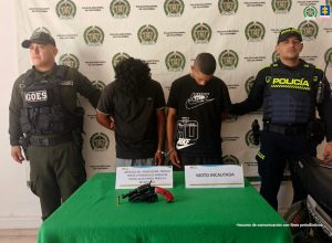En la fotografía aparecen una mujer y un hombre ambos de cabellos lisos negros, trigueños, ella vestida con camiseta beige y el con camisilla roja. Ambos están sentados asistiendo virtualmente a la audiencia en la que se les procesó. 