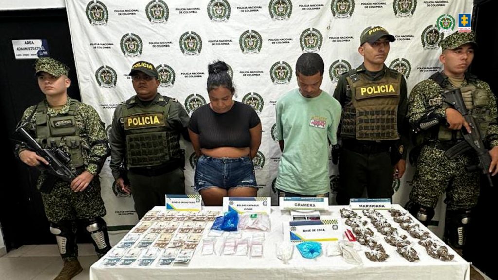 En la foto se ve a una mujer de contextura gruesa vestida con una bermuda de jean y una camiseta negra y a un hombre delgado vestido con una camiseta verde claro. Ambos se encuentran de pie con los brazos atrás esposados y custodiados por uniformados de la Policía Nacional.
