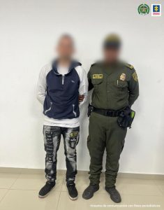 En la fotografía aparece un hombre con un buzo azul oscuro con blanco, jean gris, tenis negro, custodiado por un agente de la Policía Nacional.