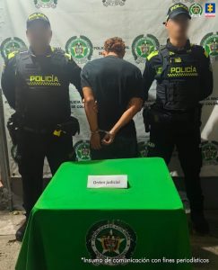 En la fotografía está un hombre de espalda con las manos esposadas, vestido con una camiseta negra y un jean azul acompañado de dos uniformados de la Policía Nacional. 