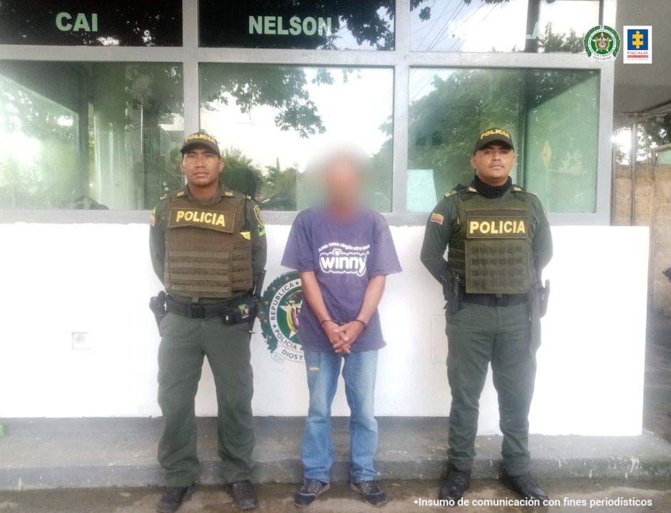 En la imagen aparece un hombre con camiseta morada y un jean custodiado por dos agentes de la Policía Nacional en un CAI de la Policía Nacional.