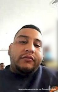 En la imagen está un hombre moreno, de contextura gruesa, cabellos negros, semi barba, cachetes pronunciados, se encuentra vestido con una camiseta azul oscura y está al interior de una oficina donde asistió virtualmente a la audiencia en la que se le judicializó. 