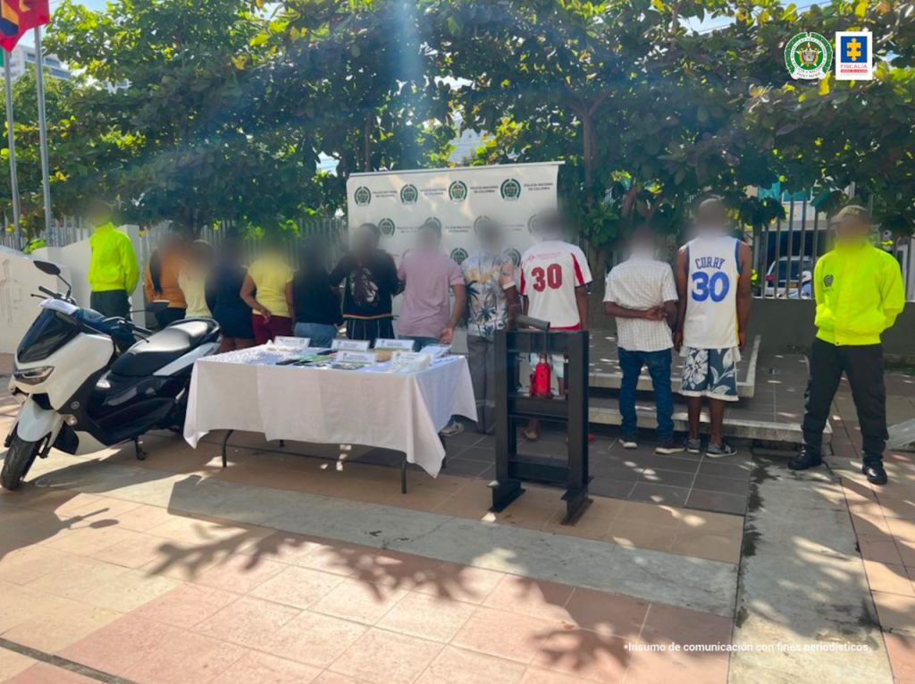 En la fotografía se observan a los capturados de espalda, custodiados por dos agentes de la Policía Nacional, delante una mesa blanca con el estupefaciente y una motocicleta incautada.