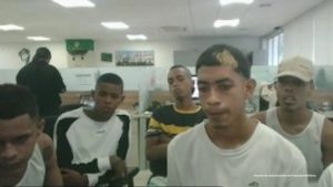En la imagen está un grupo de hombre jóvenes sentado en el interior de una oficina asistiendo virtualmente a la audiencia en la que se le procesó.