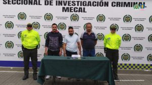 En la fotografía aparecen de pie y esposados tres de los presuntos integrantes de Los Manaos.  A lado y lado de ellos hay uniformados de la Policía Nacional. Delante de ellos hay una mesa con mantel verde y sobre ella hay cuatro celulares y un letrero que dice: ‘Celular incautado’. Detrás de ellos hay un pendón institucional de la Policía.