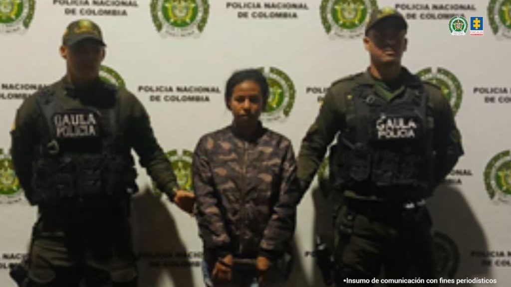 En la fotografía se aprecia de pie, con los brazos adelante y esposada a Valentina Grueso Triviño. Viste con un buso camuflado y lycra negra a las rodillas. A sus extremos hay uniformados del Gaula de la Policía Nacional. Detrás de ellos hay un pendón institucional de la Policía.