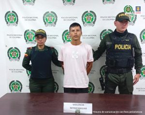 En la fotografía se aprecia de pie y con los brazos atrás a Frank David Molina Osorio. Viste camiseta de manga corta rosada y pantalón oscuro. Al lado y lado de él hay uniformados de la Policía Nacional. Delante de ellos hay una superficie marrón y sobre ella un letrero que dice: ’Violencia intrafamiliar’. En la parte de atrás de ellos hay un pendón institucional de la Policía Nacional.