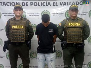 En la fotografía se aprecia de pie, con los brazos atrás y la cabeza agachada a Hanser Hawer Cruz. Viste camiseta negra de manga corta, bermuda de jean de color azul claro, desgastada. A lado y lado de él hay uniformados de la Policía Nacional. Detrás de ellos hay un pendón institucional de la Policía.