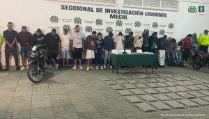 En la fotografía aparecen de pie los presuntos integrantes del grupo delincuencial Hechiceros. A los extremos de ellos hay uniformados de la Policía Nacional. Delante de ellos hay una mesa con mantel verde y sobre ella se parecían cuatro letreros. Asimismo, hay bolsas plásticas y lo que podría ser un arma de fuego. Asimismo, en el suelo hay bolsas plásticas con contenido verdoso. A lado y lado hay dos motocicletas. Detrás de ellos hay un pendón institucional de la Policía.