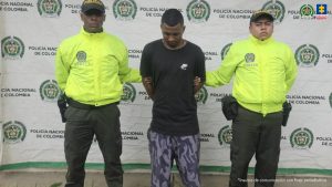 Se aprecian dos fotografías, en una de ellas hay tres hombres, uno de ellos de espaldas a la cámara. Uno viste camiseta blanca de manda ziza, bermuda negra y zapatillas blancas; otyro viste camiseta de manga corta blanca, jean azul uy zapatillas blancas con negro y el tercero buso azul con capucha, jean azul claro y zapatos negros. A los extremos hay uniformados de la Policía Nacional y en la parte posterior hay un pendón institucional de la Policía. En la fotografía 2 hay un hombre que viste camiseta negra de manga corta y vermuda gris con manchas negras y zapatos negros. A sus extremos hay uniformados de la Policía y detrás de ellos hay un pendón de la Policía.