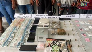 En la fotografía se aprecia una superficie blanca y sobre ella hay dinero en efectivo, celulares, pesas, munición, un proveedor y estupefacientes. Asimismo, hay varios letreros que dicen: ‘Dinero incautado’, ‘Elementos para dosificación’, ‘Marihuana’, ‘Munición’.