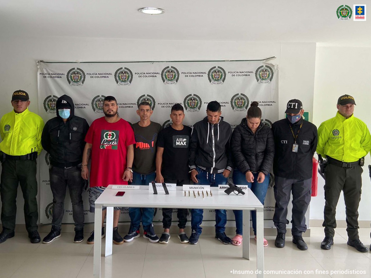 Aparecen los presuntos integrantes del grupo delictivo ‘Los Flacos Nueva Alianza’. Al lado derecho e izquierdo de ellos hay uniformados de la Policía Nacional. Delante de ellos hay una mesa blanca y sobre ella varios elementos como un arma de fuego, dos proveedores, munición y un teléfono celular. Detrás de ellos hay un pendón institucional de la Policía.