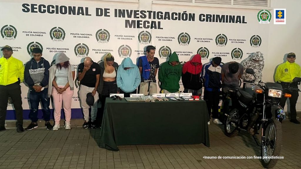 En la fotografía se aprecian los presuntos integrantes del grupo delincuencial Los WW. A lado y lado de ellos hay uniformados de la Policía Nacional. Delante de ellos hay una mesa con elementos y letreros; asimismo a la izquierda de ellos hay una motocicleta. Detrás de ellos hay un pendón institucional de la Policía.