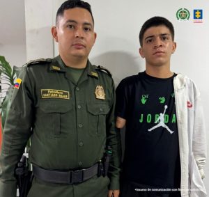 En la fotografía aparece de pie Darío Johan Montoya Valencia. Viste camiseta de manga corta, de color negro; a la altura del pecho estampado con la palabra ‘Jordan’ y figuras de color verde; bermuda de color negro y un buso blanco. Al lado derecho de él hay un uniformado de la Policía Nacional.