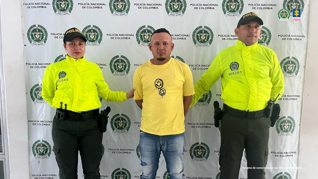 En la imagen aparece una persona de suéter amarillo entre dos uniformados de la Policía.