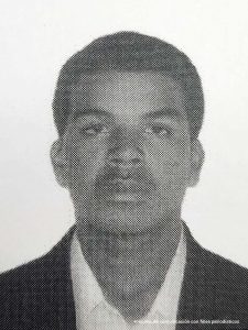 En la foto a blanco y negro está el rostro de un hombre moreno, joven, de ojos, nariz y orejas medianas, boca gruesa, cabellos negros crespos, vestido con saco negro, camisa blanca. #HayJusticia