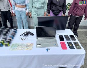 En la fotografía 2 se ve una superficie blanca y sobre ella se parecían sellos, escarapelas, dinero en efectivo, un arma de fuego y munición. En la fotografía 3 se ve una superficie blanca y sobre ella hay una pantalla, un computador portátil, celulares, una USB, dinero en efectivo, munición y un arma de fuego.