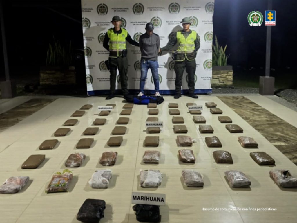 En la fotografía se aprecia de pie y con los brazos atrás a Wiston Caicedo Araujo. Usa gorra y viste con buso de color gris, jean azul desgastado y zapatillas blancas con rojo. A sus extremos hay uniformados de la Policía Nacional. En el piso hay varios paquetes envueltos en papel y plástico y sobre algunos de ellos hay letreros que dicen: ‘Marihuana’. En la parte posterior, detrás del judicializado y los policías hay un pendón institucional de la Policía.