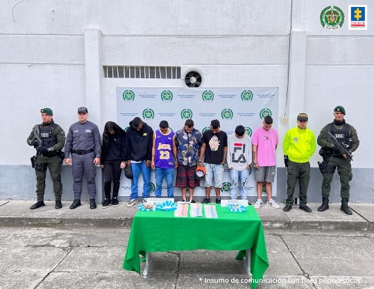 En la foto aparecen de pie y la cabeza agachada los presuntos integrantes de ‘Los Chingas’. Al lado derecho de ellos hay dos uniformados del CTI y la Policía. Al lado izquierdo hay dos uniformados de la Policía. Detrás de ellos hay un pendón institucional de la Policía Nacional.