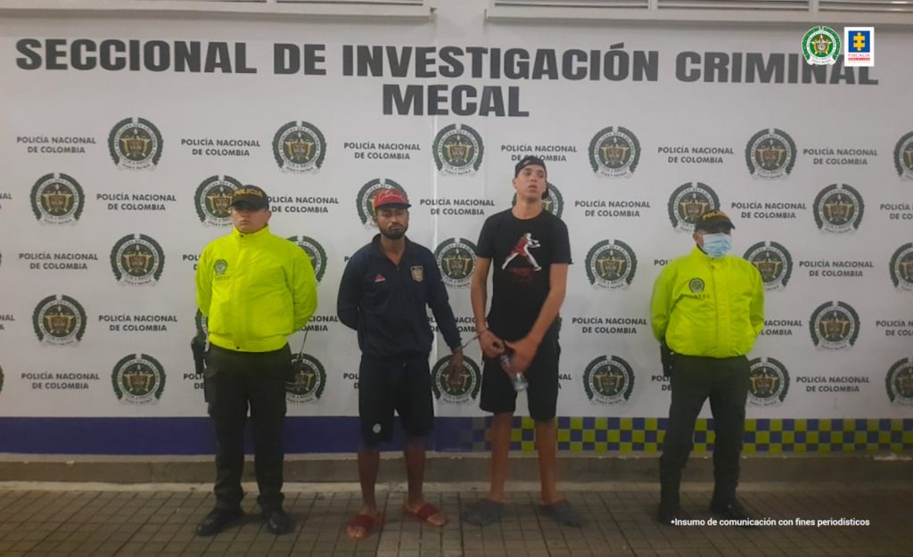 En la fotografía se aprecia a Andrés Felipe Guevara Vanegas, alias Barbas y Albert Daniel Misal Araya, alias Muelas. Amboas están de pie y esposados entre sí. Uno viste camiseta de manga corta negra con estampado de una figura saltando, a la altura del pecho; bermudas y pantuflas negras; asimismo, gorra negra con la vicera hacia atrás. El otro imputado vista chaqueta y bermuda negras, pantuflas rojas y gorra roja con negro. A lado y lado de ellos hay uniformados de la Policía Nacional. Detrás de ellos hay un pendón institucional de la Policía.