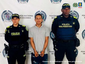 En la fotografía se aprecia de pie, con los brazos adelante y esposado a Yohan Stiven Castillo Imbachí. Viste camisa demanga corta de color gris, jean azul oscuro. A sus extremos hay uniformados de la Policía Nacional. Delante de ellos hay una superficie  de colores beige y marrón y sobre ella hay un letrero que dice: ‘Captura con orden judicial’. Detrás de ellos hay un pendón institucional de la Policía.