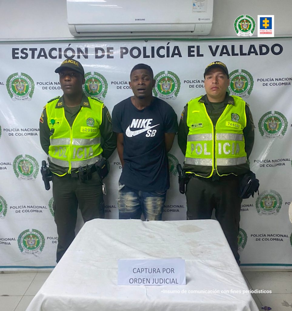 En la fotografía se aprecia a David Fabián Cuero Victoria, de pie y con los brazos atrás. Viste camiseta de manga corta negra con estampado blanco que dice: ‘Nike SB’; jean azul desgastado. A lado y lado de él hay uniformados de la Policía Nacional. Frente a ellos hay una mesa con mantel blanco y verde, sobre ella hay un letrero que dice: ‘Captura orden judicial’. Detrás de ellos hay un pendón institucional de la Policía.