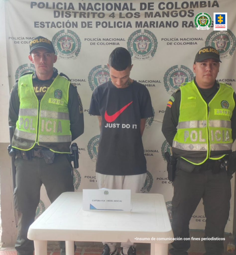 En la fotografía se aprecia a Cristian Camilo Salazar Priedrahita, de pie, con los brazos atrás y la cabeza agachada. Viste camiseta de manga corta de color negro, con estampado rojo a la altura del pecho y una frase en inglés que dice: ‘Just do it’; asimismo, pantalón blanco. A lado y lado de él hay uniformados de la Policía Nacional. Delante de ellos hay una mesa blanca cuadrada y sobre ella hay un letrero que dice: ‘Captura por orden judicial’. En la parte posterior hay un pendón institucional de la Policía.