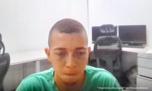 En la fotografía aparece la imagen de un hombre joven, moreno, vestido de camiseta verde. Se encuentra sentado en una oficina atendiendo la audiencia virtual donde fue judicializado.