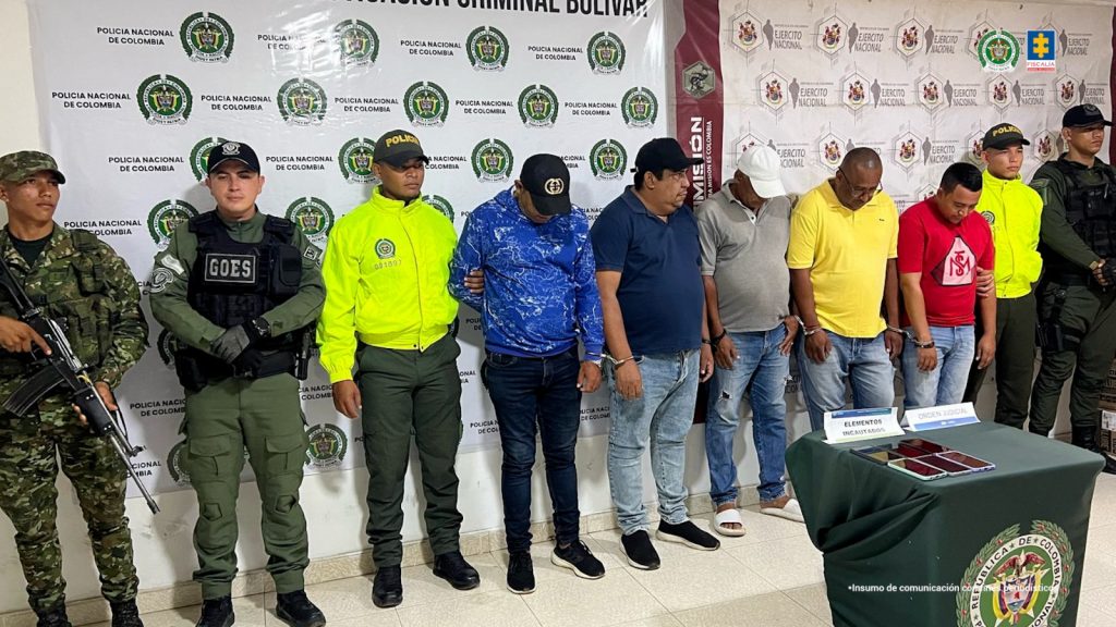 En la fotografía están los cinco procesados de pie, esposados y custodiados por uniformados de la Policía y el Ejército Nacional. 