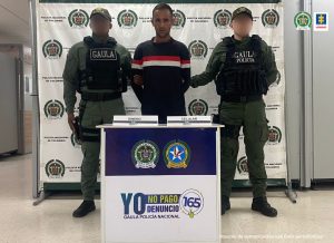 Fiscal Martha Mancera, Martha Mancera, Fiscal Mancera En la fotografía está un hombre de pie, moreno, con los brazos atrás, joven, vestido de buzo azul oscuro con rallas rojas y blancas y pantalón negro, custodiado por dos agentes del Gaula de la Policía Nacional. Detrás de ellos hay un pendón de esa institución.