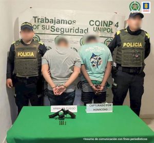 En la fotografía aparecen dos hombres de espalda, con las manos esposadas, uno vestido de camiseta gris con jean azul y el otro de camiseta azul marino con bermuda verde con rallas blancas y negras, custodiados por dos uniformados de la Policía Nacional.